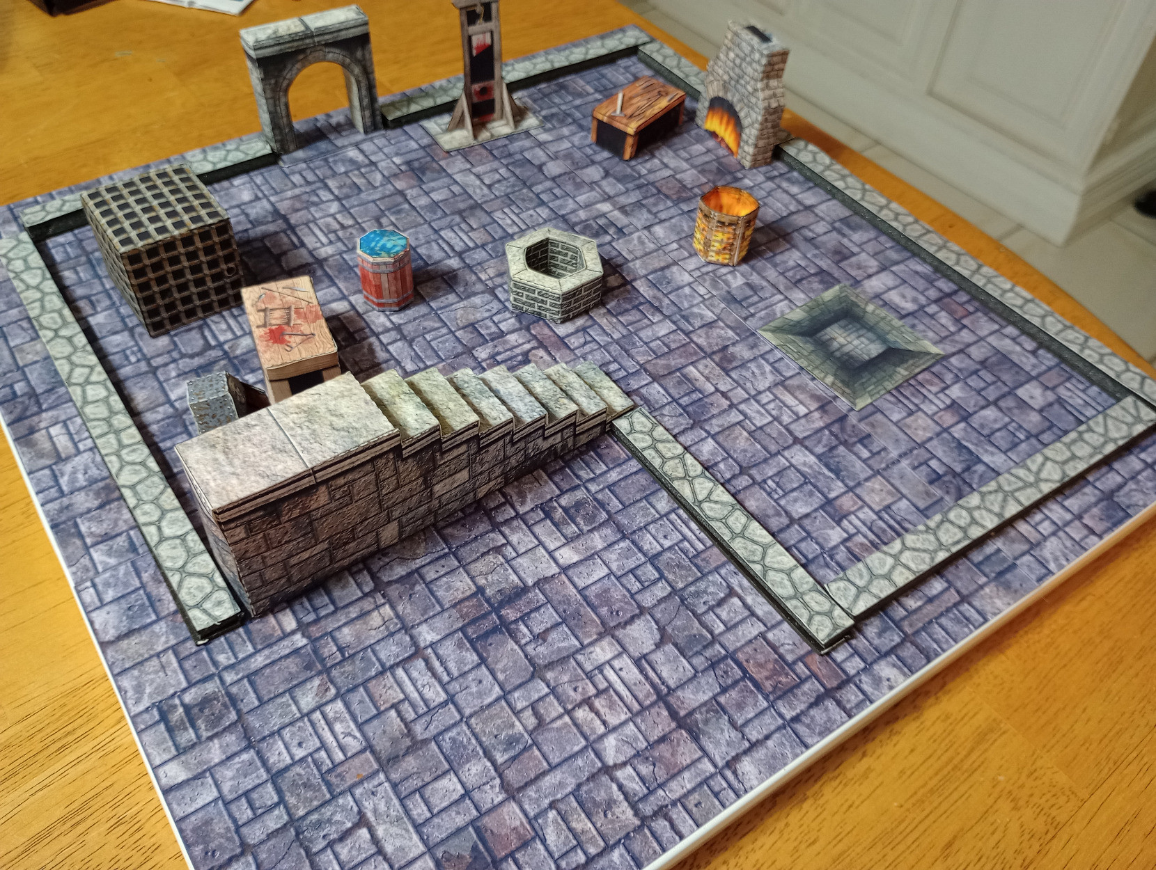 A square board covered with printed paper dungeon tiles. A bunch of paper scenery making a dungeon room, attched to the board with magnets.