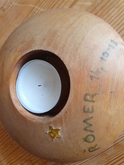 Teelichthalter rund aus Holz, ziemlich flach, mit benutzten Teelicht und der Aufschift: 