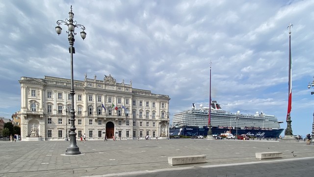 A large cruise ship docked at the cruise terminal of the port of Trieste and a historic building of the Piazza Unita d‘Italia at Trieste. The position of the shot is chossen so that it looks like the ship id docked at the palazzo.