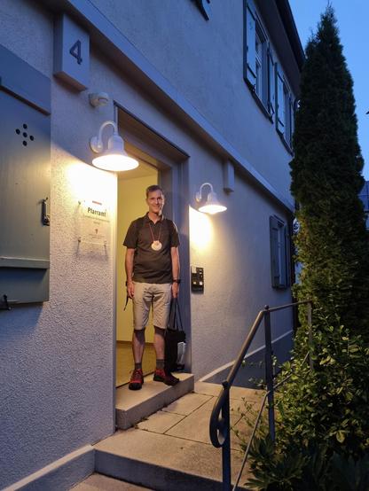 Ich mit Pilgermuschel um den Hals an der geöffneten Haustür stehend.