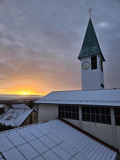 Kirchturm mit Schnee und Sonnenaufgang