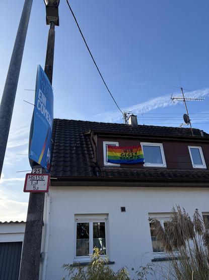 Haus mit Pride Flagge geschmückt auf der steht „wir gehen rechts.“ an der Laterne vor dem Haus hängen Wahlplakate der Faschisten.