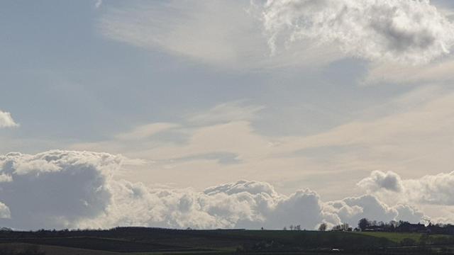 Wolken und blauer Himmel über einer Landschaftssilhouette am unteren Bildrand