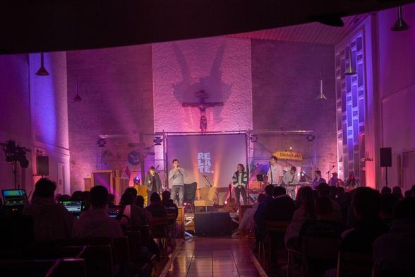 Lila erleuchtete Kirche von innen mit aufgebauter Bühne und Schriftzug Relate