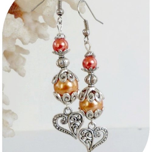 Boucles d'oreilles perles nacrées oranges et breloques cœurs et crochets argentés.