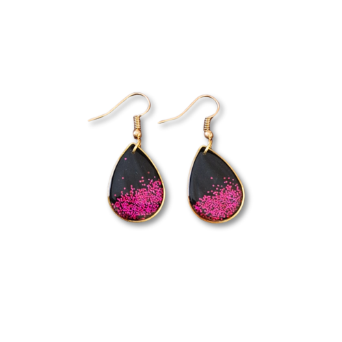 Boucles d'oreilles goutte en polymère noir, son bord doré et ces paillettes fuchsia