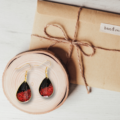 Boucles d'oreilles goutte en polymère noir, son bord doré et ces paillettes rouges