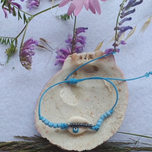 Bracelet ajustable en coton ciré bleu turquoise cauri oeil turc agrémenté de perles de rocaille noires et bleues ciel.