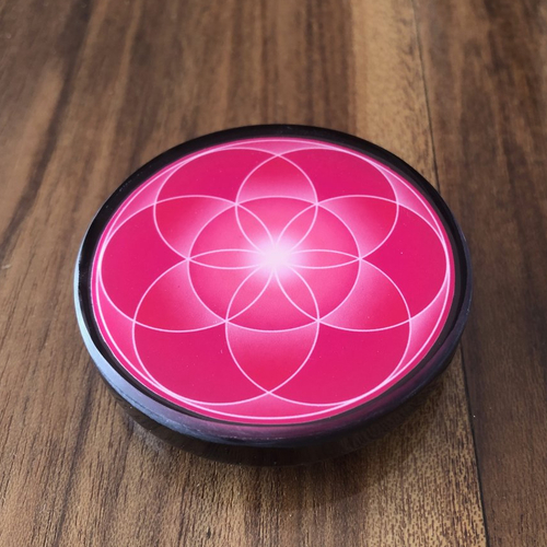 Plaque 6.50cm en shungite, graine de vie en recto, et fleur de vie au verso. symbole de renouveau. couleur rose, chakra du cœur.
