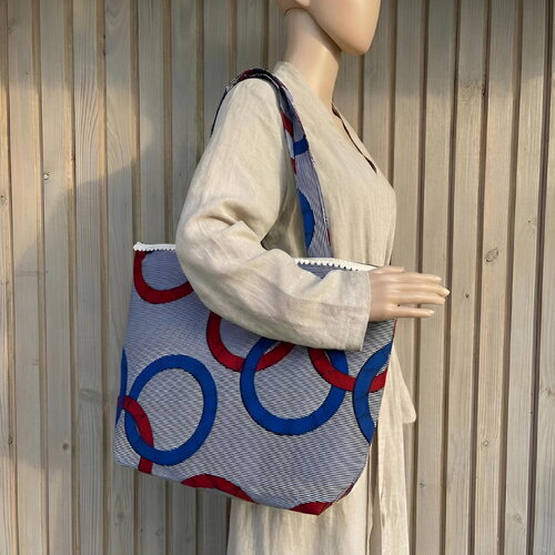 Sac cabas en wax porté épaule motif géométrique bleu et rouge avec ponpoms