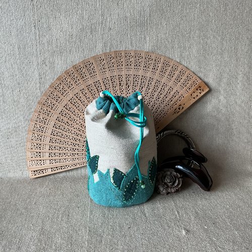 Pochette boule en soie sauvage écrue et décor de feuillage dans différents verts.