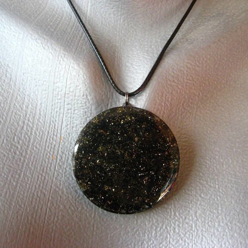 Pendentif unisexe monté sur un cordon noir cailloux noirs et dorés sur fond transparent en résine diamètre 40mm