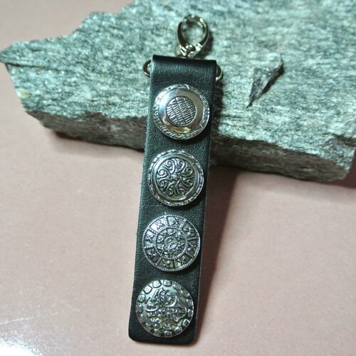 Un porte-clés homme 4 boutons pression snap en métal argenté sur support en cuir noir 14,5 x 3,1 cm