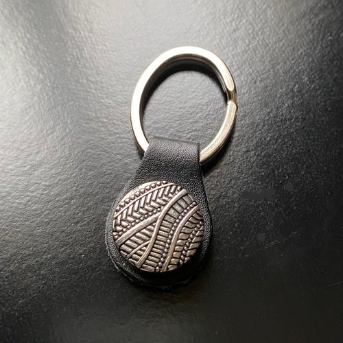 Un porte-clés 6,5 cm, cuir noir et anneau ovale, bouton snap 20 mm décor géométrique en métal argenté