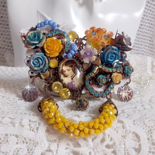 Broche eclats pétillants d’inspiration baroque ornée de fleurs, dentelle, breloques, cristaux, perles sur estampes laiton et métal.