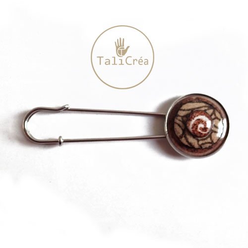 Une épingle à nourrice argentée spirale en sables rouges, jaunes, marron
