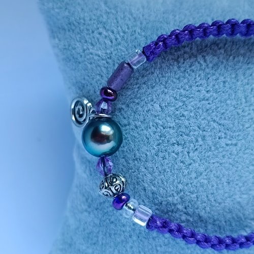 Joli bracelet en coton peigné violet composé d'une magnifique perle de tahiti, de breloques argentées et de perles de rocaille violettes.